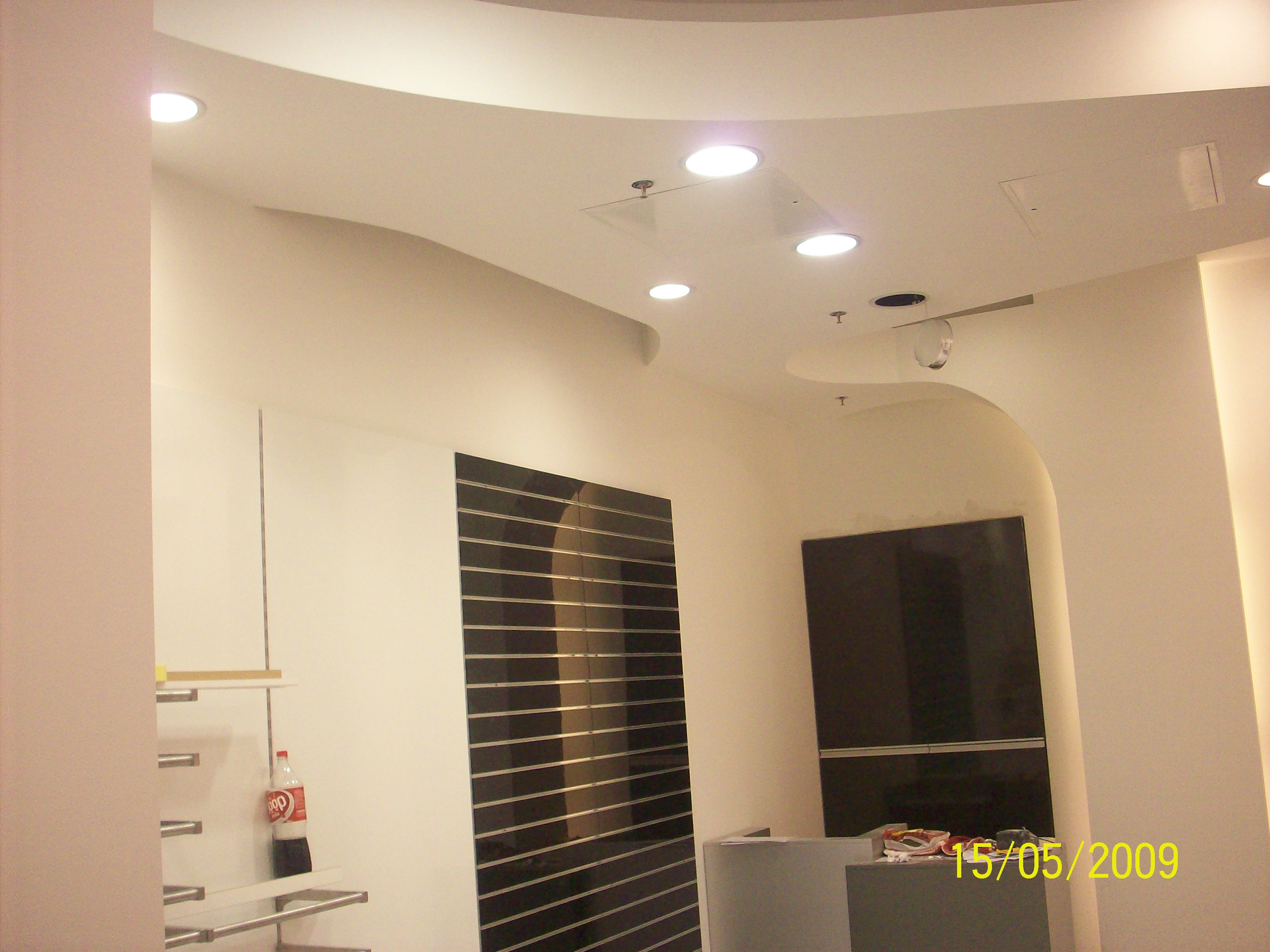 Wnętrze sklepu w trakcie remontu: widoczne fragmenty ścian z zabudową G/K, oświetlenie sufitowe, regały i fragment lady.